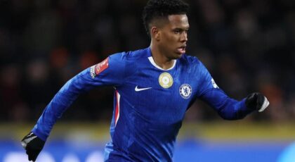 Jogador de futebol Estêvão. Homem negro, cabelo black, usando uniforme azul do Chelsea no campo jogando futebol.