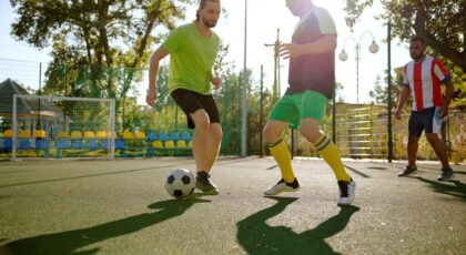 Homens jogando futebol em quadra com o sol batendo.