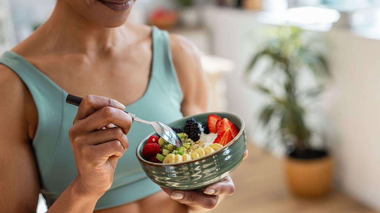Imagem de uma pessoa comendo iogurte com frutas picadas em um pote
