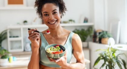 Imagem de uma mulher, com roupa de academia, comendo frutas e iogurte