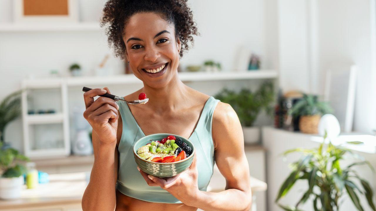 Imagem de uma mulher, com roupa de academia, comendo frutas e iogurte