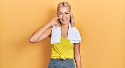 Imagem de uma mulher com roupa de academia e uma toalha nos ombros apontando para sua bochecha