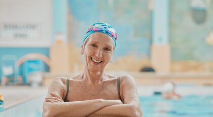 Mulher idosa sorrindo dentro da piscina fazendo natação.