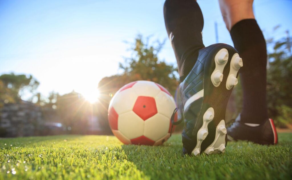 Foto mostra um pé jogando bola no campo de futebol.