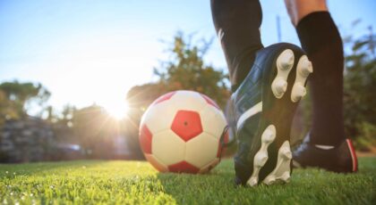 Foto mostra um pé jogando bola no campo de futebol.