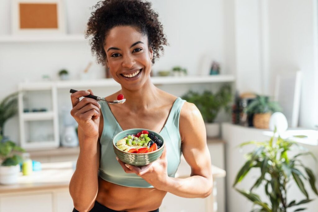 Mulher com roupa de academia comendo um bowl na cozinha.