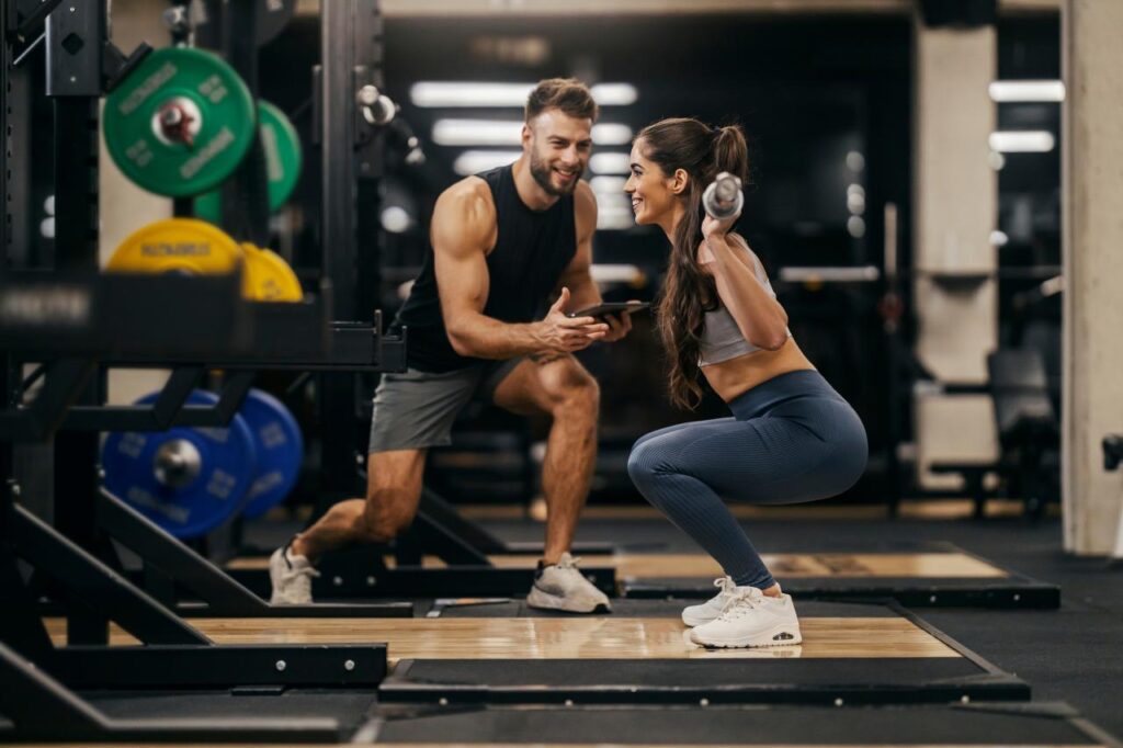 Mulher fazendo exercício físico na academia com um treinador do lado.