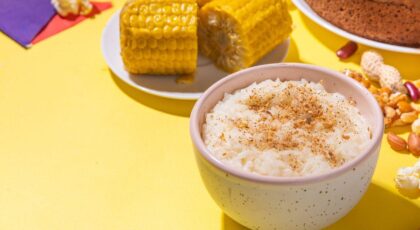 Imagem de arroz doce com canela em um pote, duas espigas de milho e um bolo redondo