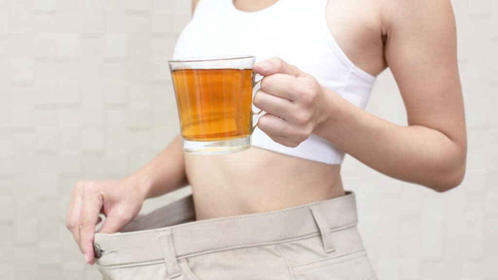 Imagem de uma mulher segurando uma xícara de chá e mostrando a calça larga na cintura