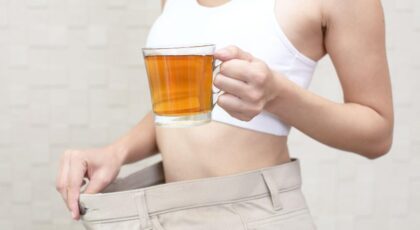 Imagem de uma mulher segurando uma xícara de chá e mostrando a calça larga na cintura