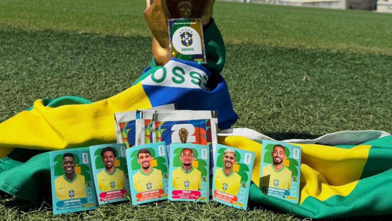 Imagem das figurinhas da Copa encostadas em uma bandeira do Brasil e na taça da Copa no estádio