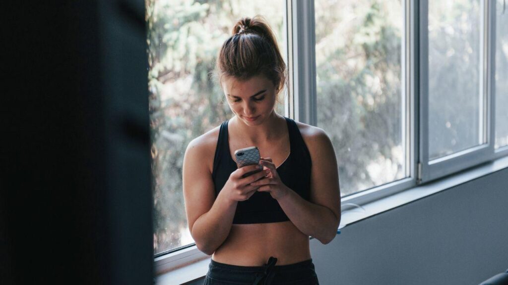 Imagem de uma mulher com roupa de treino mexendo no celular