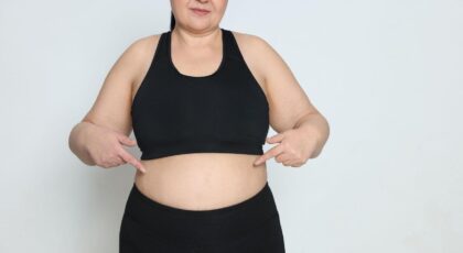 Imagem de uma mulher plus size apontando para a barriga vestindo top e legging pretos