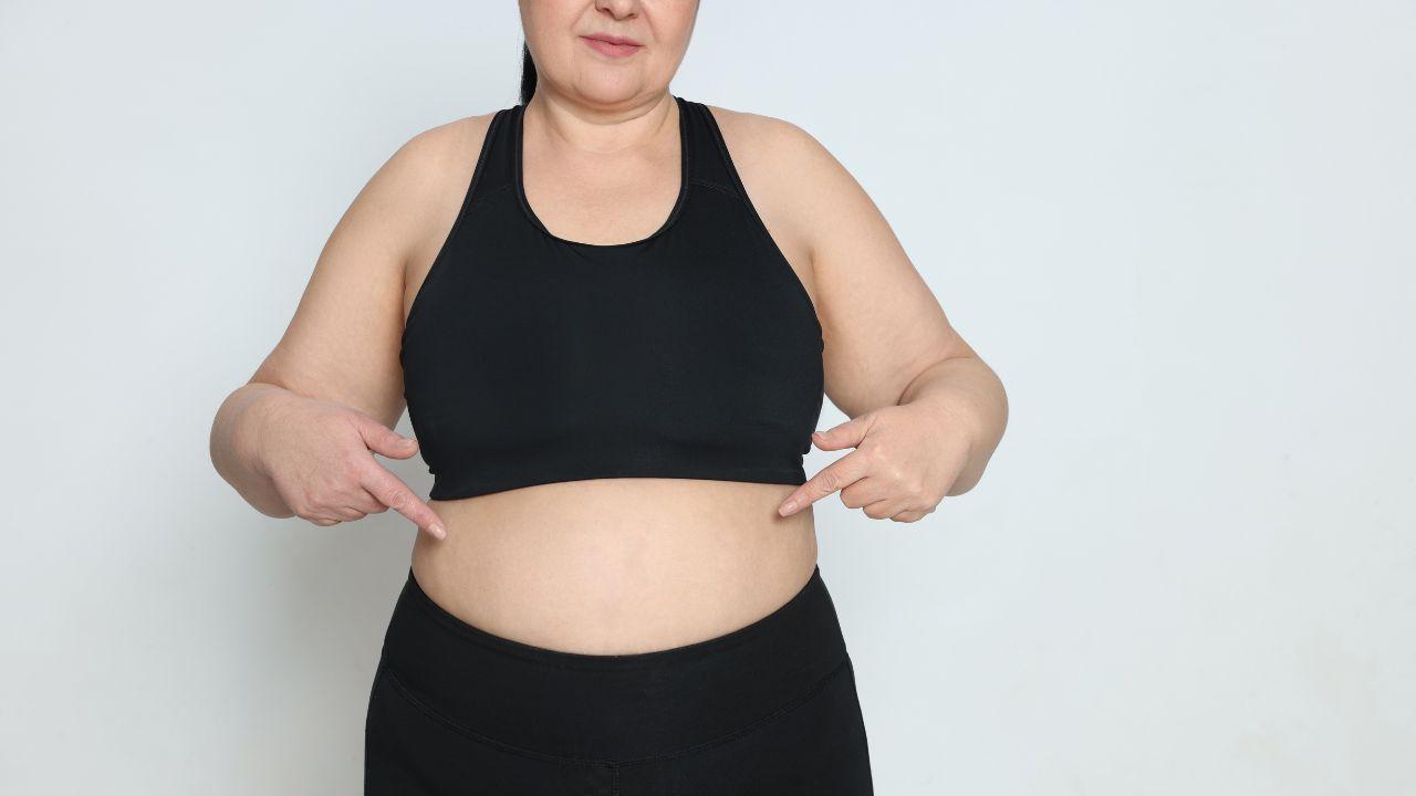 Imagem de uma mulher plus size apontando para a barriga vestindo top e legging pretos
