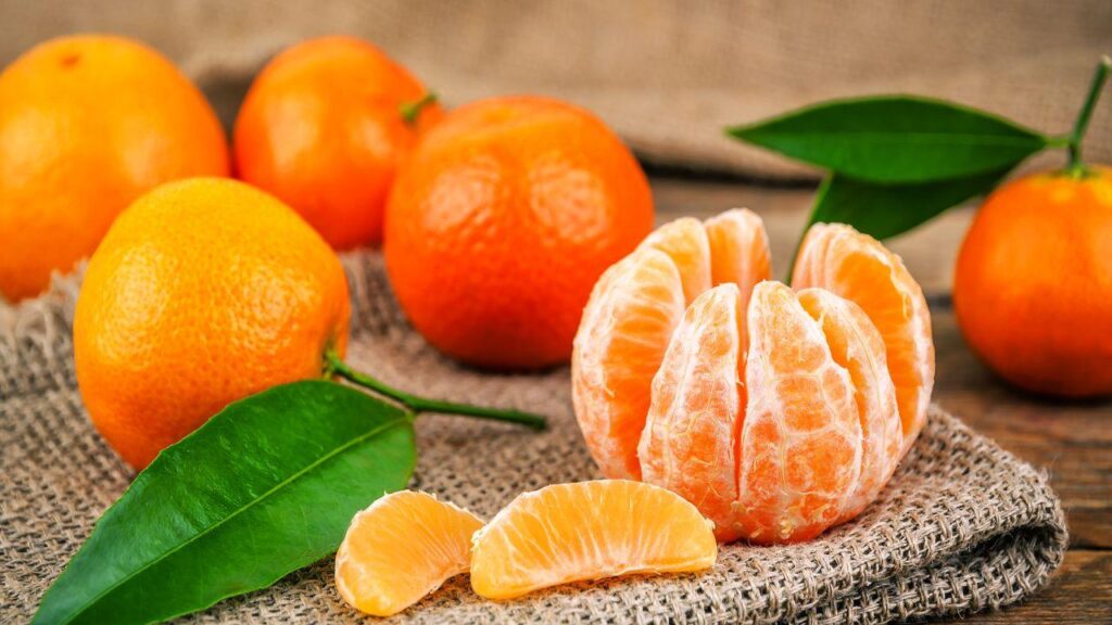 Imagem de uma tangerina descascada e algumas tangerinas com casca atrás