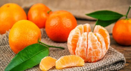 Imagem de uma tangerina descascada e algumas tangerinas com casca atrás
