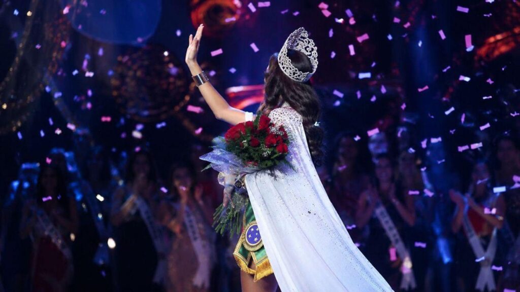 Foto mostra uma miss no palco fazendo o tchauzinho de miss.