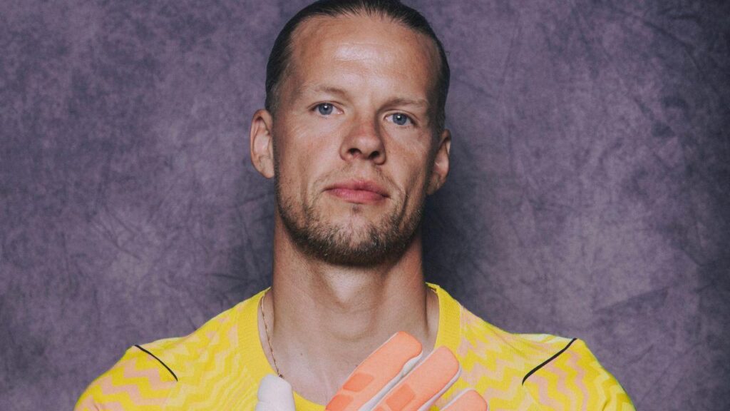 Foto mostra Ørjan Nyland. Homem branco, olhos claros, loiro, cabelo amarrado para trás, usando luvas de goleiro.