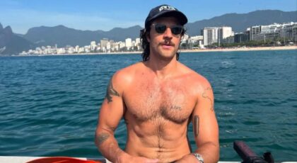Chay Suede. Homem branco, cabelo curto castanho, sem camisa, abdômen definido, usando boné, barba e bigode ao ar livre.