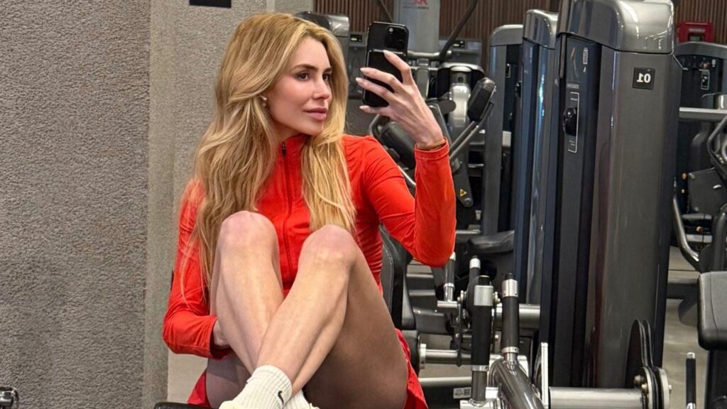 Foto mostra a influenciadora Joana Cabral. Mulher branca, cabelo loiro, sentada num aparelho de academia.