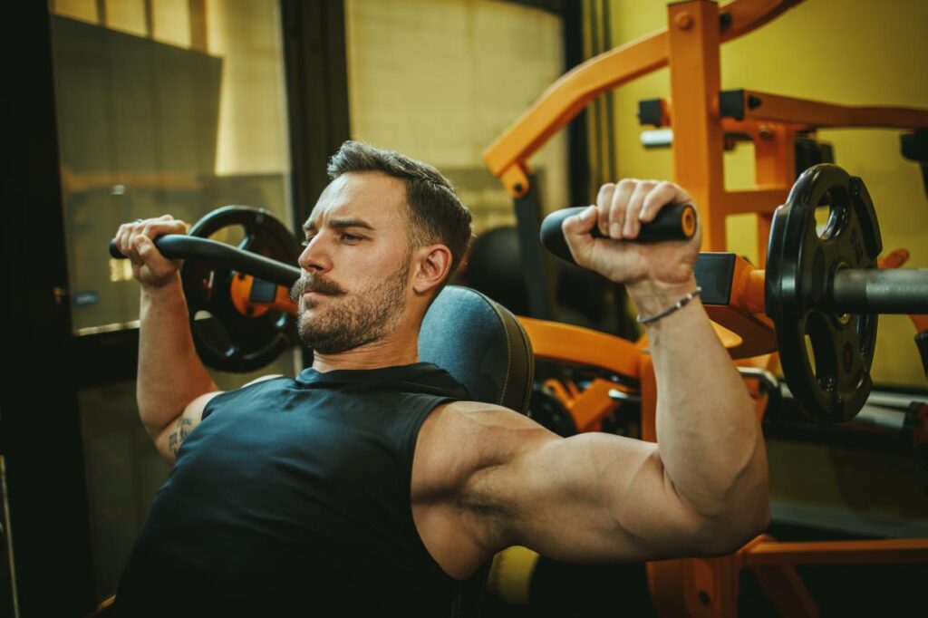 Foto mostra homem fazendo exercício de braço na academia.