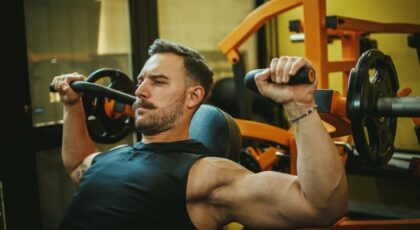 Foto mostra homem fazendo exercício de braço na academia.