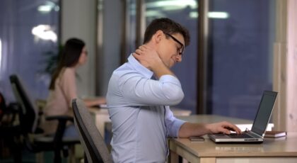 Homem sentado na cadeira do escritório torcendo o pescoço.
