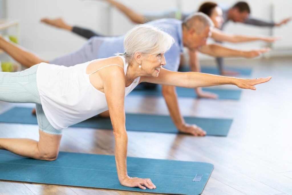 Mulheres idosas fazendo pilates solo no chão esticando os braços.