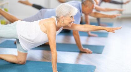 Mulheres idosas fazendo pilates solo no chão esticando os braços.