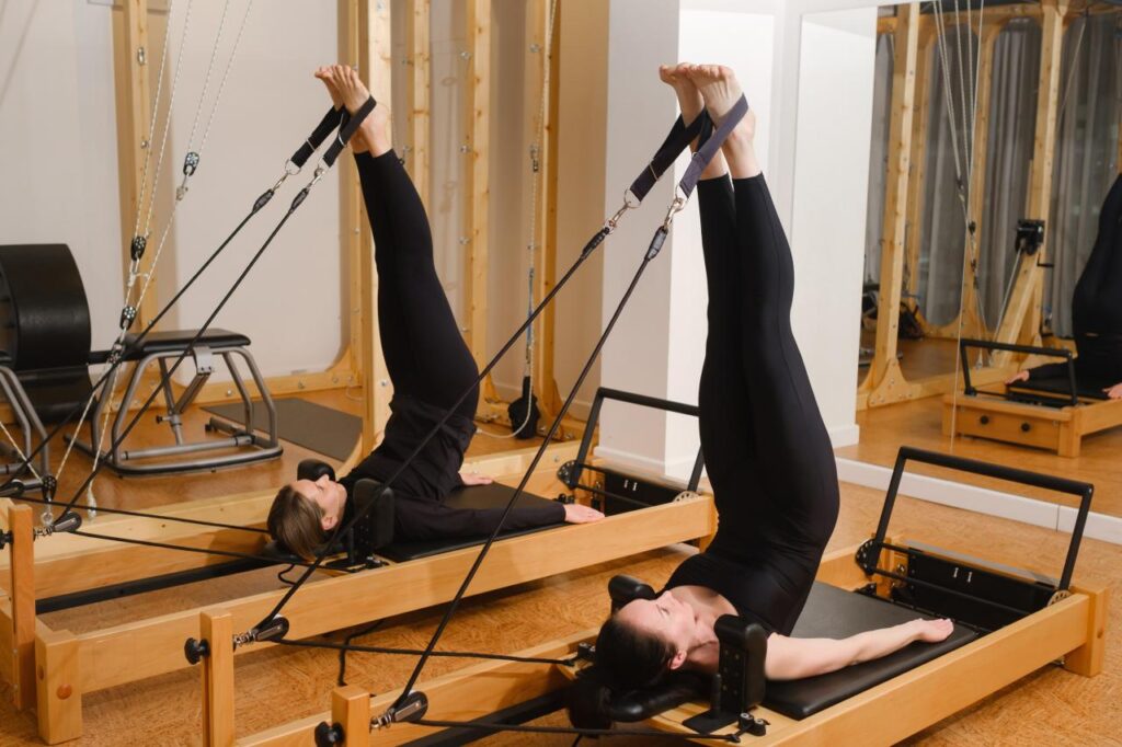 Foto mostra mulher fazendo exercício num aparelho de pilates com as pernas pra cima.