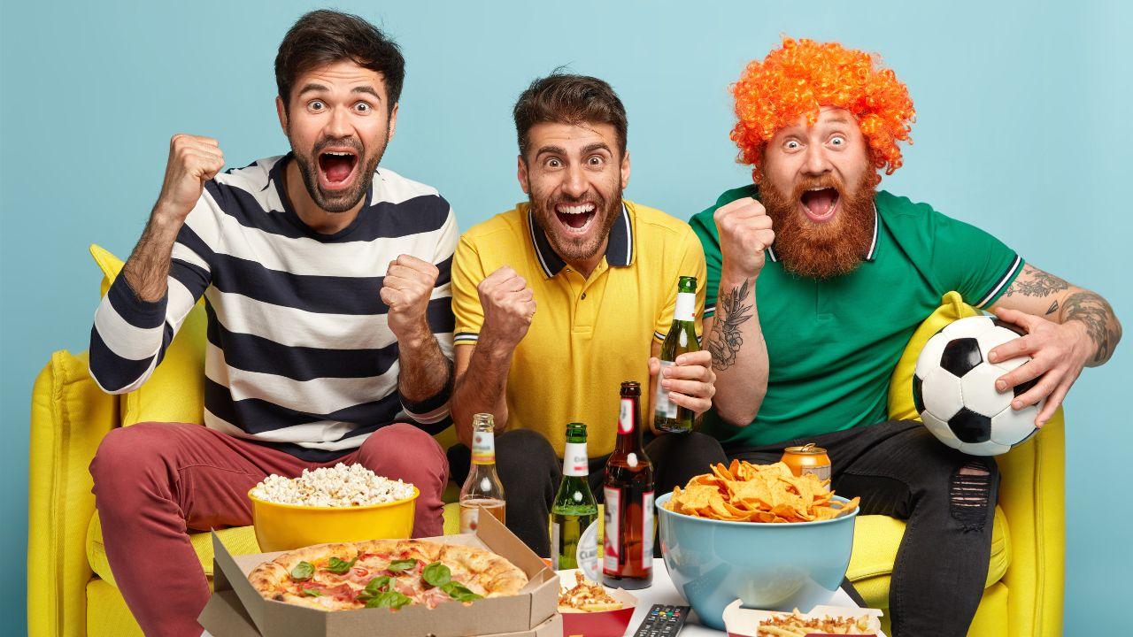 Imagem de homens torcendo e comendo besteiras