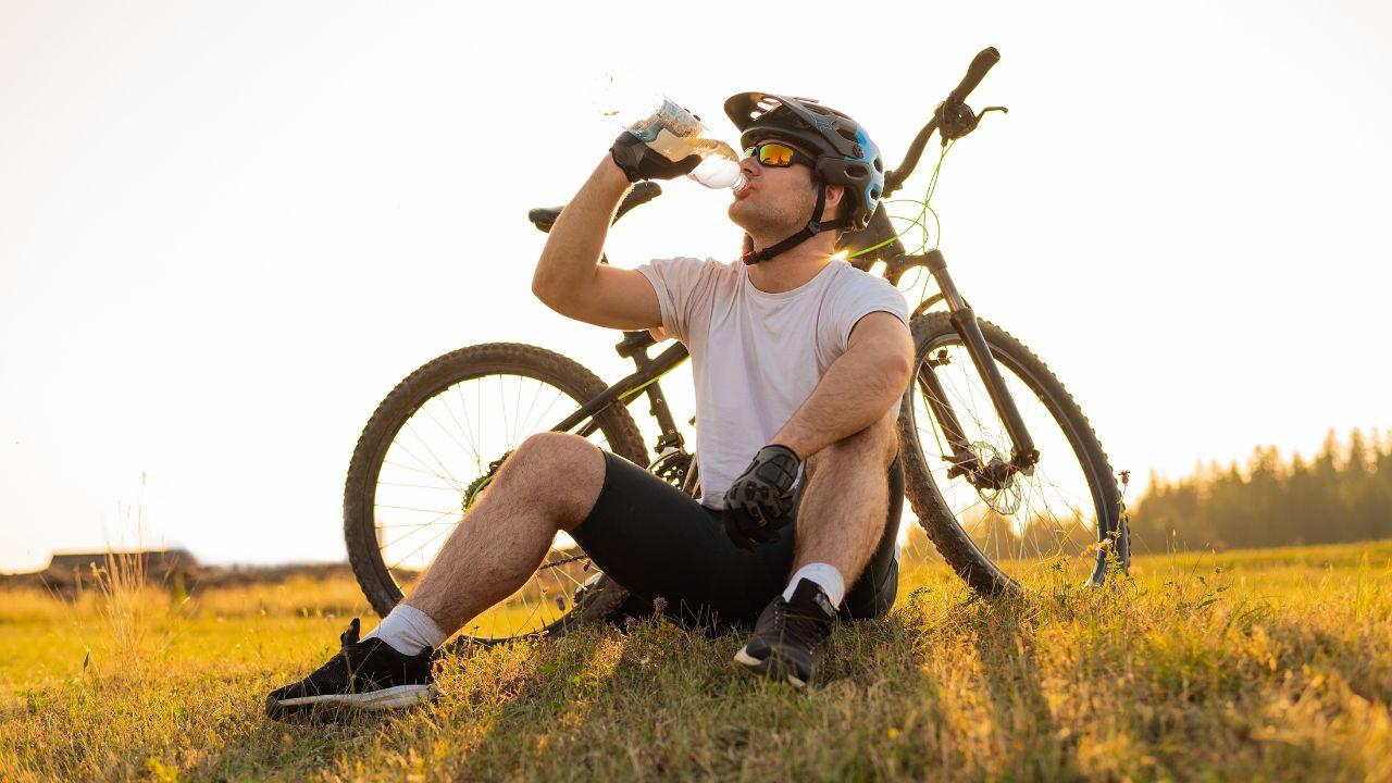 Imagem de um ciclista ao lado da bicicleta tomando água