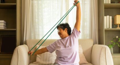 Imagem de uma idosa fazendo exercício com elástico no sofá