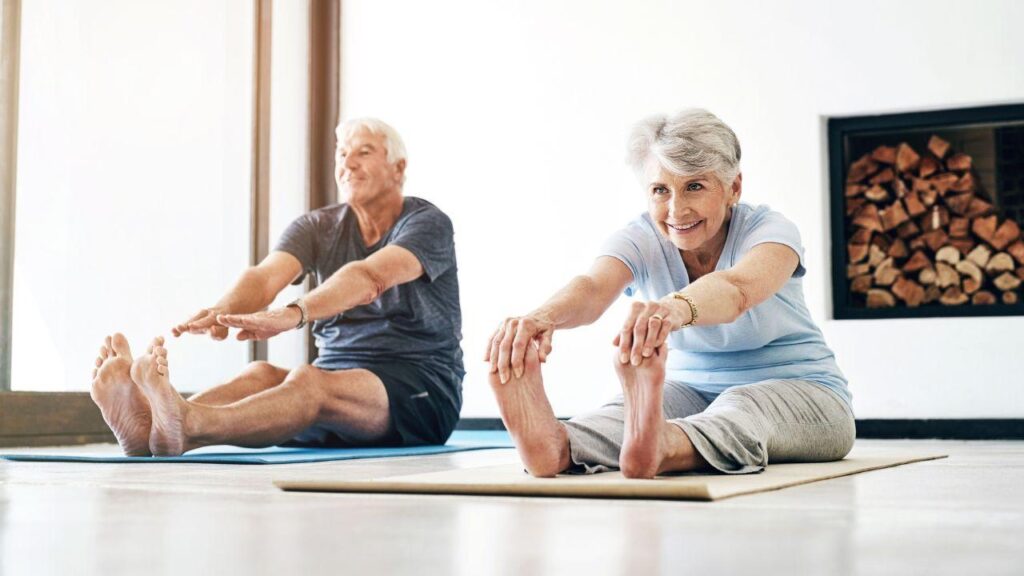 Imagem de dois idosos fazendo exercício de pilates se alongando para frente