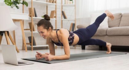 Imagem de uma mulher fazendo pilates na sala de casa em frente ao computador