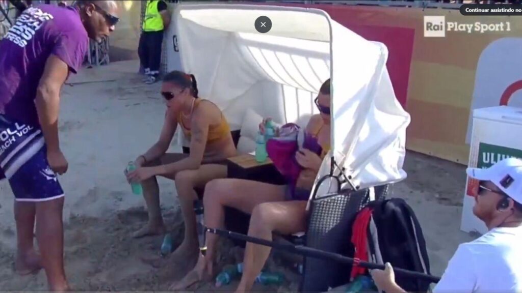 Imagem mostra o técnico em pé gritando com as jogadoras sentadas em cadeiras.