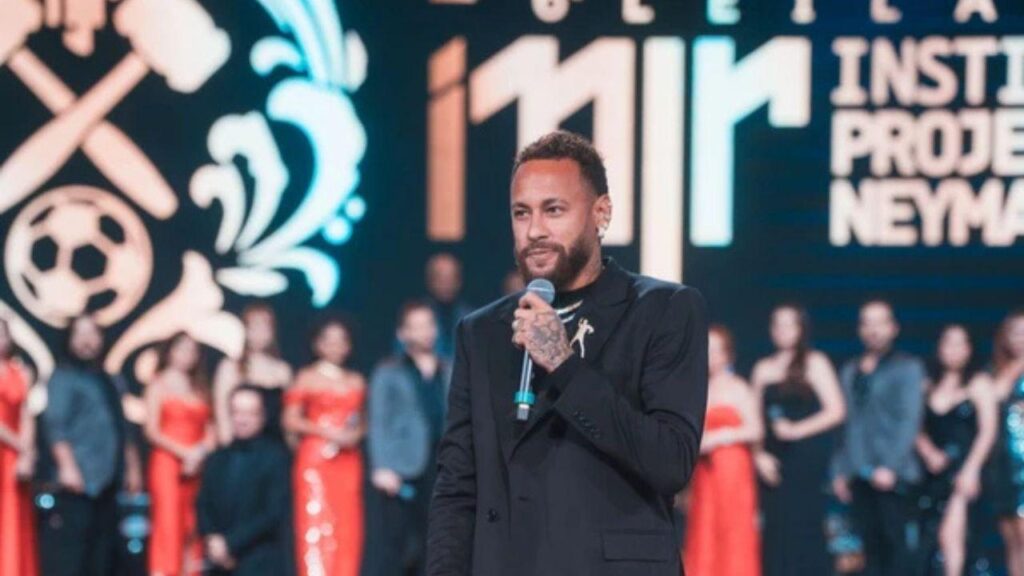 Neymar de terno preto segurando microfone no palco do leilão.