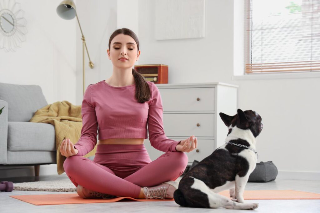 Foto mostra mulher sentada num colchonete no chão em posição de meditação.