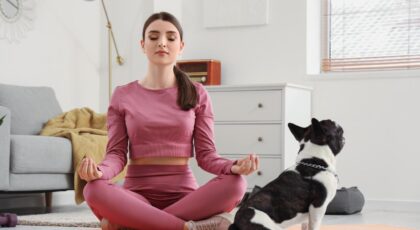 Foto mostra mulher sentada num colchonete no chão em posição de meditação.