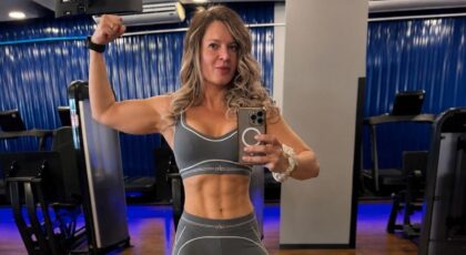 Joice Hasselmann. Mulher branca, cabelo loiro ondulado, com top cinza, tirando foto na frente do espelho com o biceps em destaque.