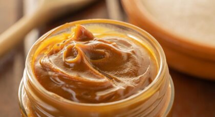 Foto mostra um pote de vidro com doce de leite pastoso e cremoso dentro.