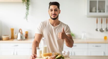 Homem na frente da bancada da cozinha com uma tábua com várias comidas nutritivas.