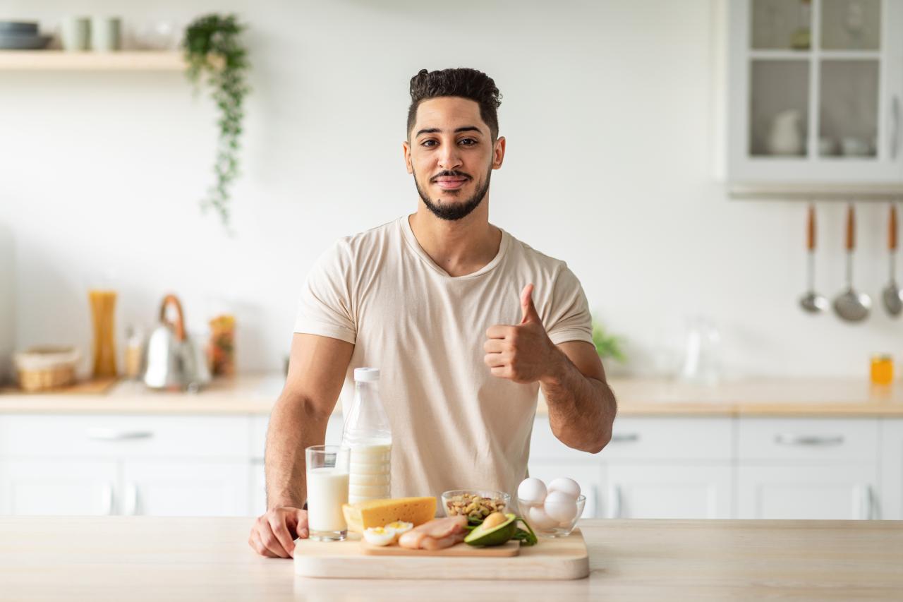 Homem na frente da bancada da cozinha com uma tábua com várias comidas nutritivas.