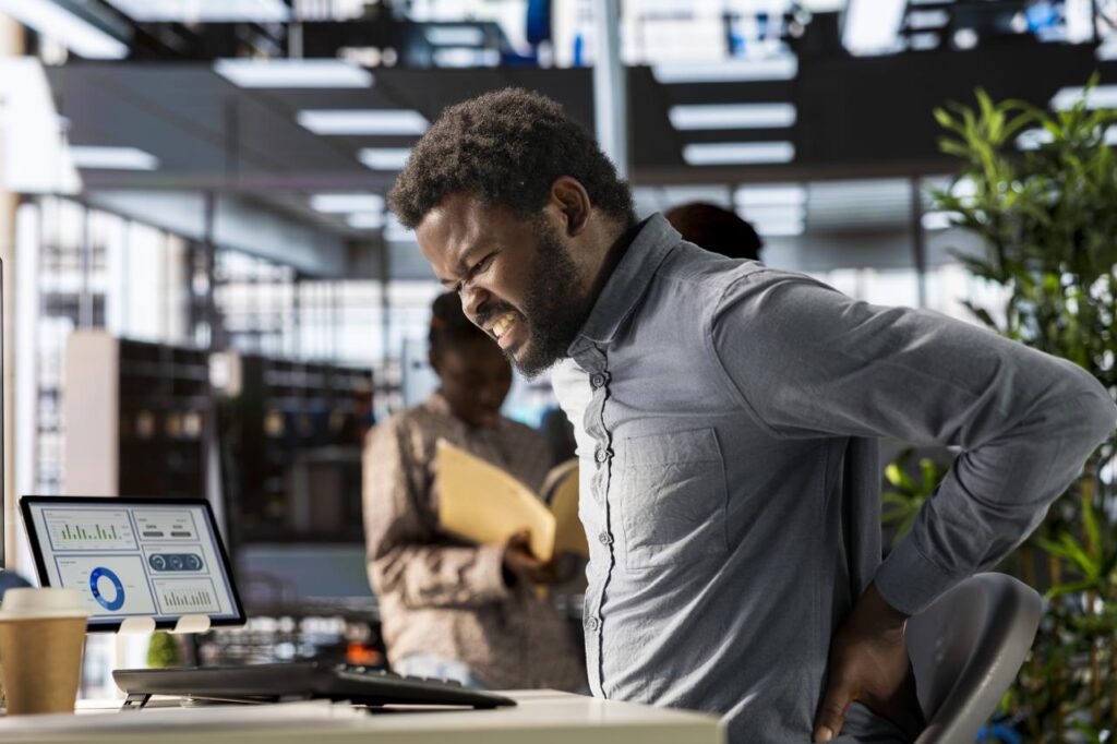 Homem negro sentado na cadeira do escritório com má postura.