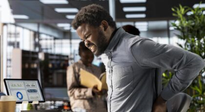 Homem negro sentado na cadeira do escritório com má postura.